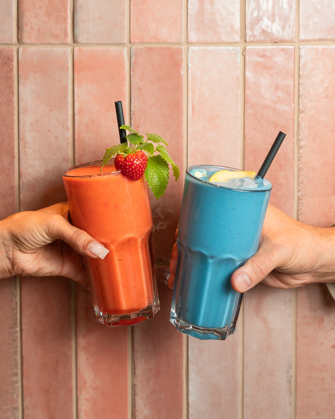 Zwei Smoothies in Orange und Blau, in Händen gehalten